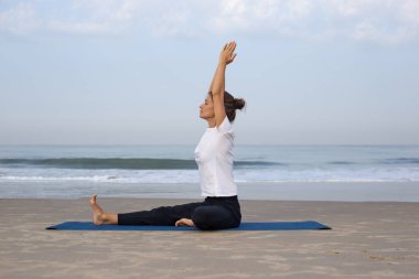 Sahilde yoga yapan genç bir kız. Beyaz elbiseli.