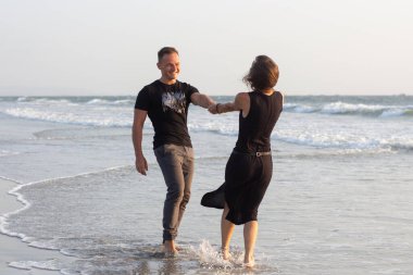 Gün batımında terk edilmiş tropik bir plajda koşan, gülen ve el ele tutuşan mutlu iki genç erkek ve kadın.