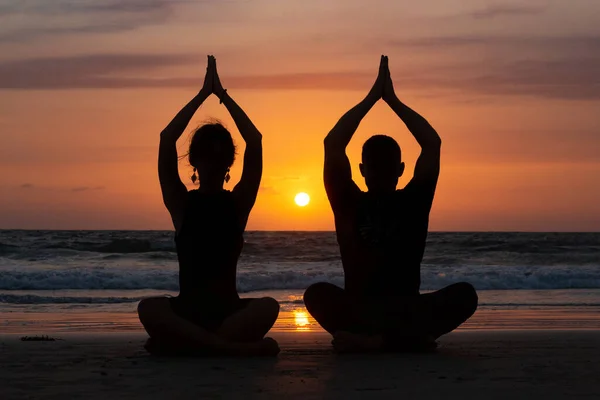 Jong paar oefenen yoga op de zee strand bij zonsondergang — Stockfoto