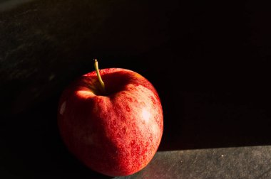 Doğal pencere ışığına sahip kırmızı elma, gölge ve siyah arkaplan oluşturur