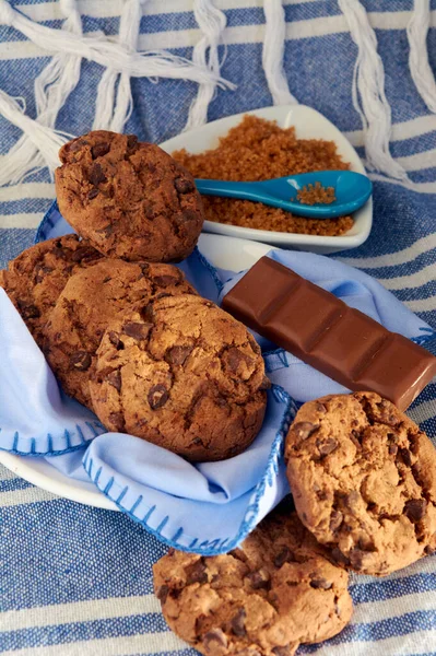 plate of cocoa cookies, brown cane sugar and chocolate, with blue tones on napkin, wooden table, tablecloth and spoon