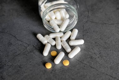 Koyu beton bir masadaki kavanozdan beyaz ve turuncu antibiyotik haplar.