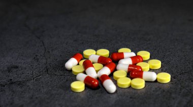 Koyu beton bir masada sarı, beyaz ve kırmızı antibiyotik haplar.