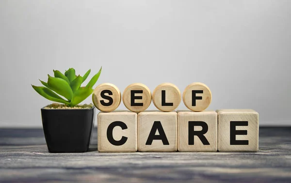 SELF CARE - ahşap küplerle ilgili metin, ahşap arka planda siyah çömlekte yeşil bitki