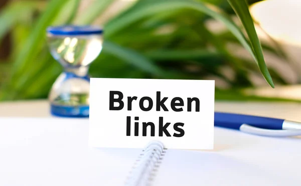 Broken links seo business concept text on a white notebook and hourglass, blue pen, green flowers
