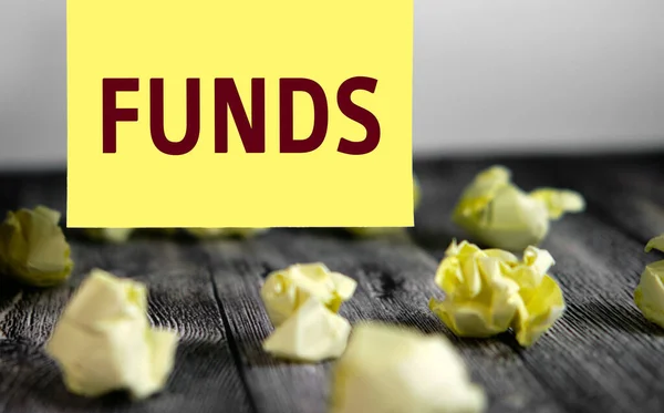 Funds - text on yellow note sheets on a dark wooden background with crumpled sheets