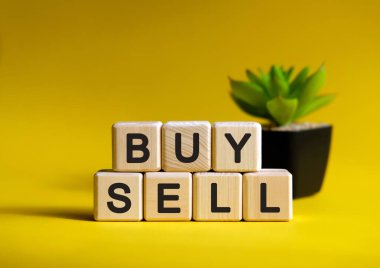 Sat ya da satın al - finansal konsept. Tahta küpler ve çiçek sarı arka planda bir tencerede.