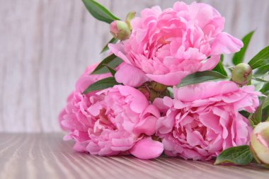 Çiçek açan bir buket pembe şakayık, ahşap arka planda yeşil yapraklı tomurcuklar.