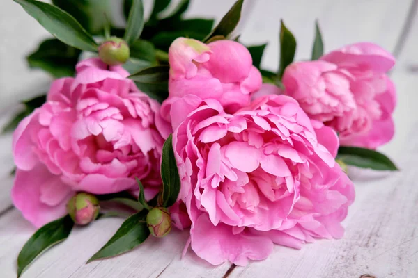 Bir buket pembe kırmızı şakayık, ahşap bir masanın üzerinde yatıyor.
