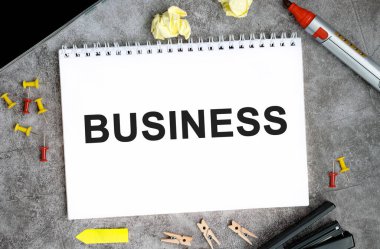 Beton bir masa üzerinde iğne, işaret ve zımba bulunan beyaz bir defterde iş konsepti metni