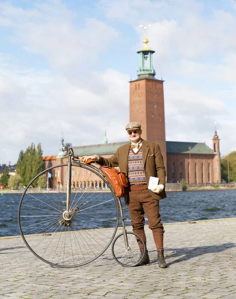 stock image STOCKHOLM - SEPT 22, 2018: Senior man wearing old fashioned tweed suit holding a high wheeler bicycle in front of Stockholm City Hall in the Bike in Tweed event September 22, 2018 in Stockholm, Sweden