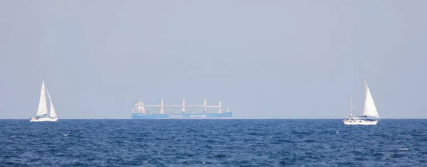 Gran barco de transporte y dos veleros en el océano azul en el — Foto de Stock