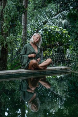 Yeşil kimonolu genç sarışın kadın orman yolunda yürüyor.