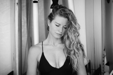 Siyah beyaz bikinili genç bir kadının portresi. Arka planda sörf tahtaları var. Gülümsüyor.