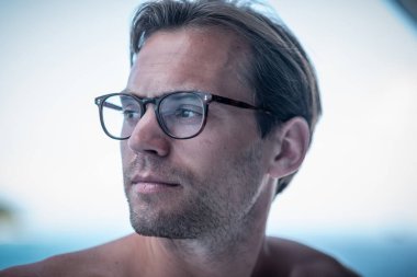 Yakışıklı üstsüz adamın portresi, şık gözlüklü sörfçü ve arka planda mavi okyanus.