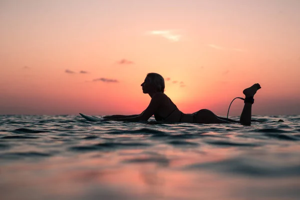 バリのカラフルな夕日の時間に海のサーフボード上の美しい体を持つサーファーの女の子の水からの肖像画 — ストック写真