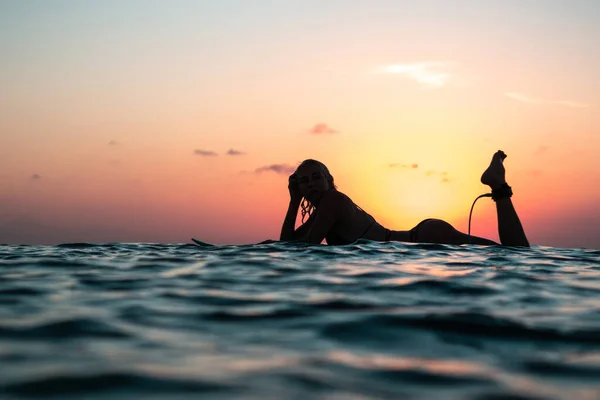 バリのカラフルな夕日の時間に海のサーフボード上の美しい体を持つサーファーの女の子の水からの肖像画 — ストック写真