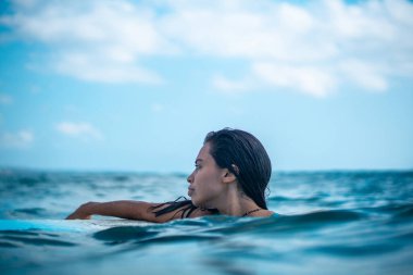 Mavi okyanusta beyaz sörf tahtasındaki sörfçü kızın portresi Bali 'deki sudan çekilmiştir.