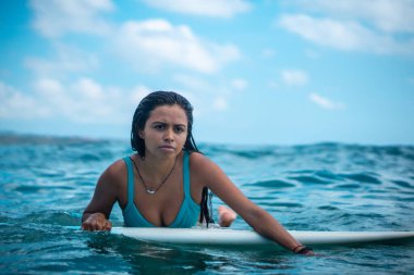 Mavi okyanusta beyaz sörf tahtasındaki sörfçü kızın portresi Bali 'deki sudan çekilmiştir.