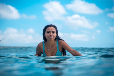 Mavi okyanusta beyaz sörf tahtasındaki sörfçü kızın portresi Bali 'deki sudan çekilmiştir.