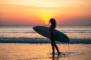 Bali 'de günbatımında sörf tahtasıyla sahilde güzel vücutlu bir kadın sörfçü portresi