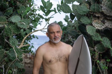 Beyaz sörf tahtası ve Bali arka planında yeşil kaktüs tutan yakışıklı sörfçü portresi.