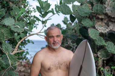Beyaz sörf tahtası ve Bali arka planında yeşil kaktüs tutan yakışıklı sörfçü portresi.