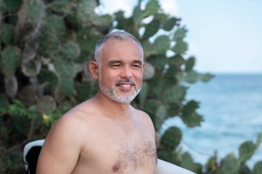 Beyaz sörf tahtası ve Bali arka planında yeşil kaktüs tutan yakışıklı sörfçü portresi.
