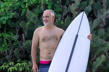 Bali 'de beyaz sörf tahtası ve kaktüs tutan yakışıklı bir sörfçünün siyah beyaz portresi.