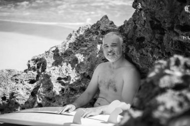 Bali 'de beyaz sörf tahtası ve kaktüs tutan yakışıklı bir sörfçünün siyah beyaz portresi.