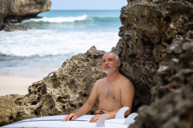 Bali 'de beyaz sörf tahtası ve kaktüs tutan yakışıklı bir sörfçünün siyah beyaz portresi.