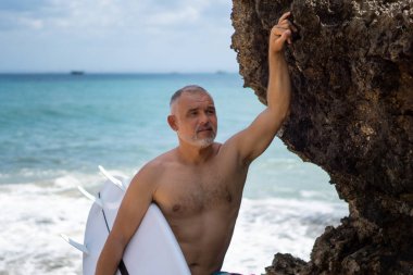 Beyaz sörf tahtası ve Bali arka planında yeşil kaktüs tutan yakışıklı sörfçü portresi.