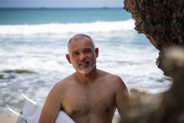 Bali 'de beyaz sörf tahtası ve kaktüs tutan yakışıklı bir sörfçünün siyah beyaz portresi.