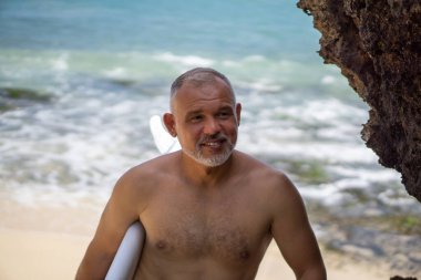 Beyaz sörf tahtası ve Bali arka planında yeşil kaktüs tutan yakışıklı sörfçü portresi.