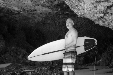 Bali 'de beyaz sörf tahtası ve kaktüs tutan yakışıklı bir sörfçünün siyah beyaz portresi.
