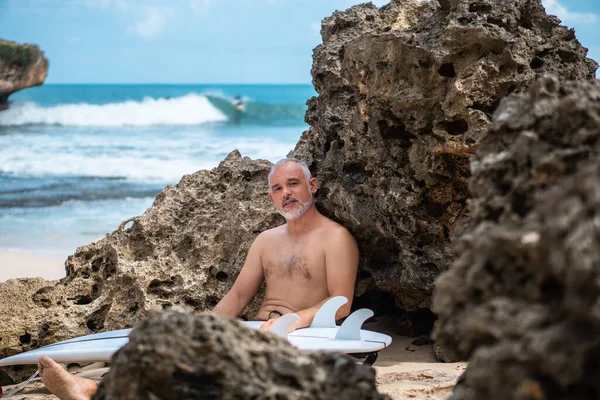 Beyaz sörf tahtası ve Bali arka planında yeşil kaktüs tutan yakışıklı sörfçü portresi.