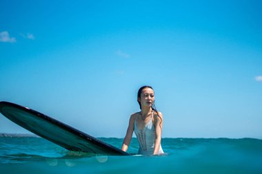 Mavi okyanusta sörf tahtasındaki sörfçü kızın portresi Bali 'deki sudan çekilmiştir.