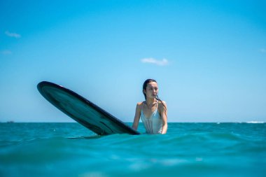 Mavi okyanusta sörf tahtasındaki sörfçü kızın portresi Bali 'deki sudan çekilmiştir.