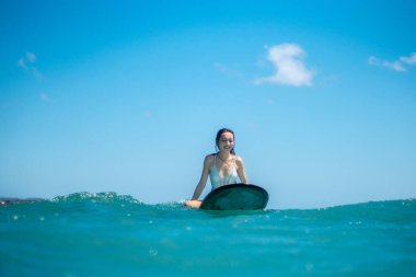 Mavi okyanusta sörf tahtasında dövmesi olan sörfçü kızın portresi Bali 'de sudan çekilmiş.