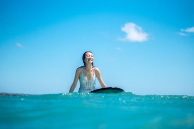 Mavi okyanusta sörf tahtasında dövmesi olan sörfçü kızın portresi Bali 'de sudan çekilmiş.