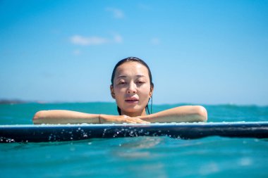 Mavi okyanusta sörf tahtasındaki sörfçü kızın portresi Bali 'deki sudan çekilmiştir.