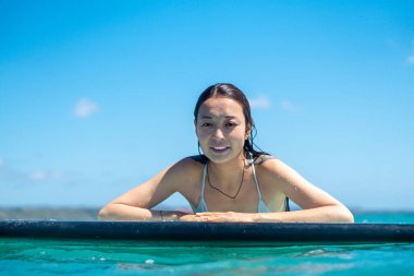 Mavi okyanusta sörf tahtasındaki sörfçü kızın portresi Bali 'deki sudan çekilmiştir.