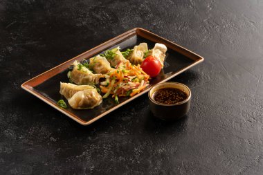 Taze sebzeli haşlanmış hamur köftesi, lahana, turp, havuç, salatalık, yeşil soğan ve susam tohumlu soya sosu. Pan-Asya ve Asya yemekleri ve yemekler şık beton mutfak masasında..