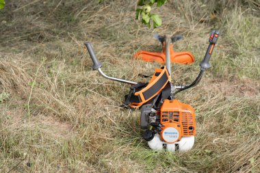 Minsk, Belarus - 02 / 08 / 2020 Petrol tırpan kesici Husqvarna 143R-II bir kır evinin bahçesindeki çimleri biçtikten sonra biçilen samanlıkta yatıyor.