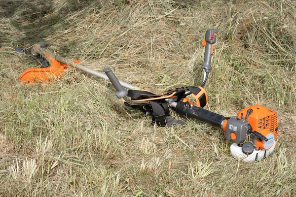 Minsk, Belarus - 02 / 08 / 2020 Petrol tırpan kesici Husqvarna 143R-II bir kır evinin bahçesindeki çimleri biçtikten sonra biçilen samanlıkta yatıyor.