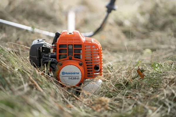 Minsk, Belarus - 02 / 08 / 2020 Petrol tırpan kesici Husqvarna 143R-II bir kır evinin bahçesindeki çimleri biçtikten sonra biçilen samanlıkta yatıyor.