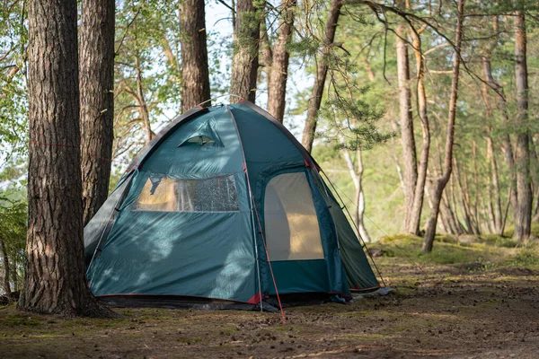 A large tourist tent is set up on the campground in a beautiful forest by the lake. Camping with a tent. Self-isolation in the forest during the COVID-19 quarantine.