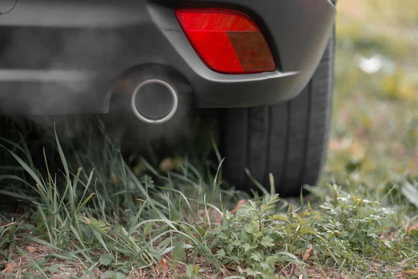 Çimlere park edilmiş bir arabanın egzoz borusundan çıkan toksik CO2 egzoz dumanı. Sığ alan derinliği, bulanık arkaplan.