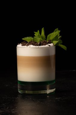 Kahve sanatı. Sütlü latte, krema, şurup, kurabiye kırıntıları ve siyah arka planda nane yaprakları.