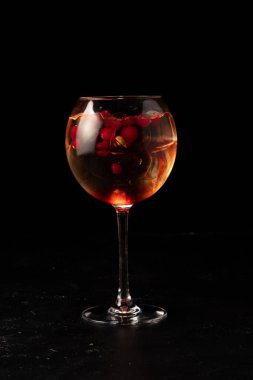 Siyah arka planda şeffaf bir bardakta yaban mersini ve böğürtlen şurubuyla alkollü kokteyl.
